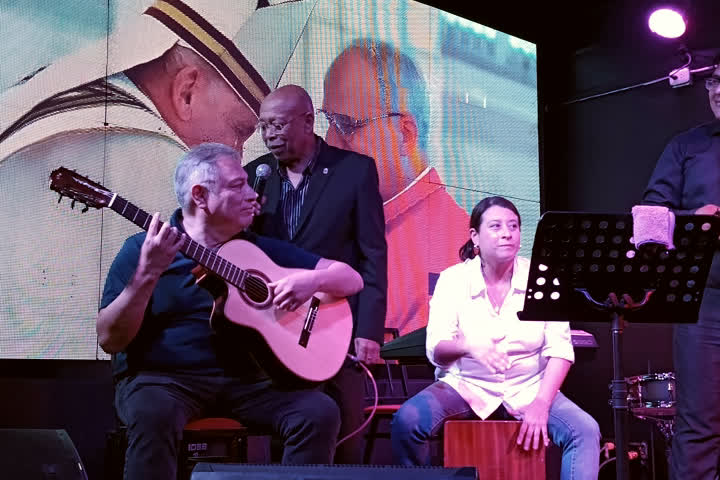 Carlos Mosquera tocando guitarra sentado, junto a otros músicos.